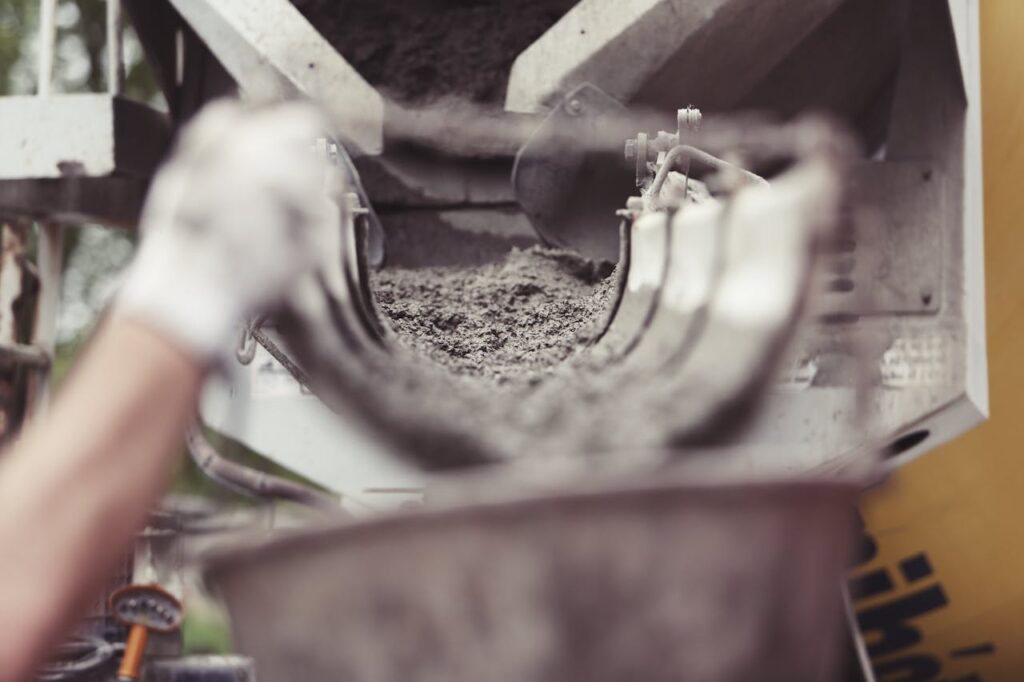 building-construction-building-site-constructing Close-up of concrete being poured from a mixer truck at a construction site with a worker's hand visible.