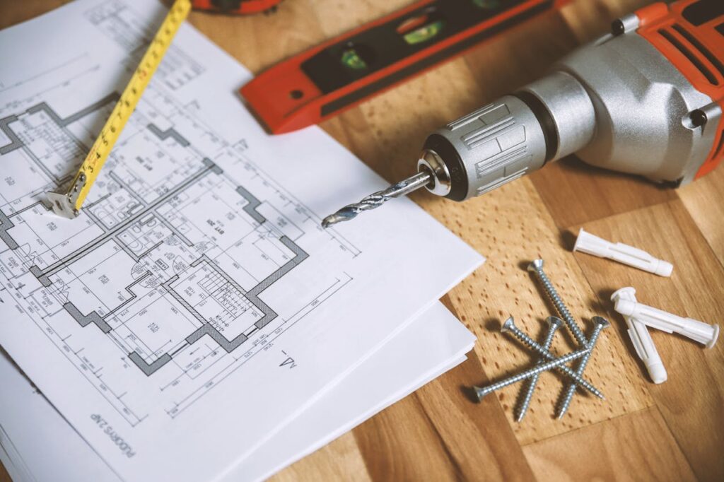 pexels-photo-834892 Close-up of construction blueprint with tools like drill and screws on a wooden table.